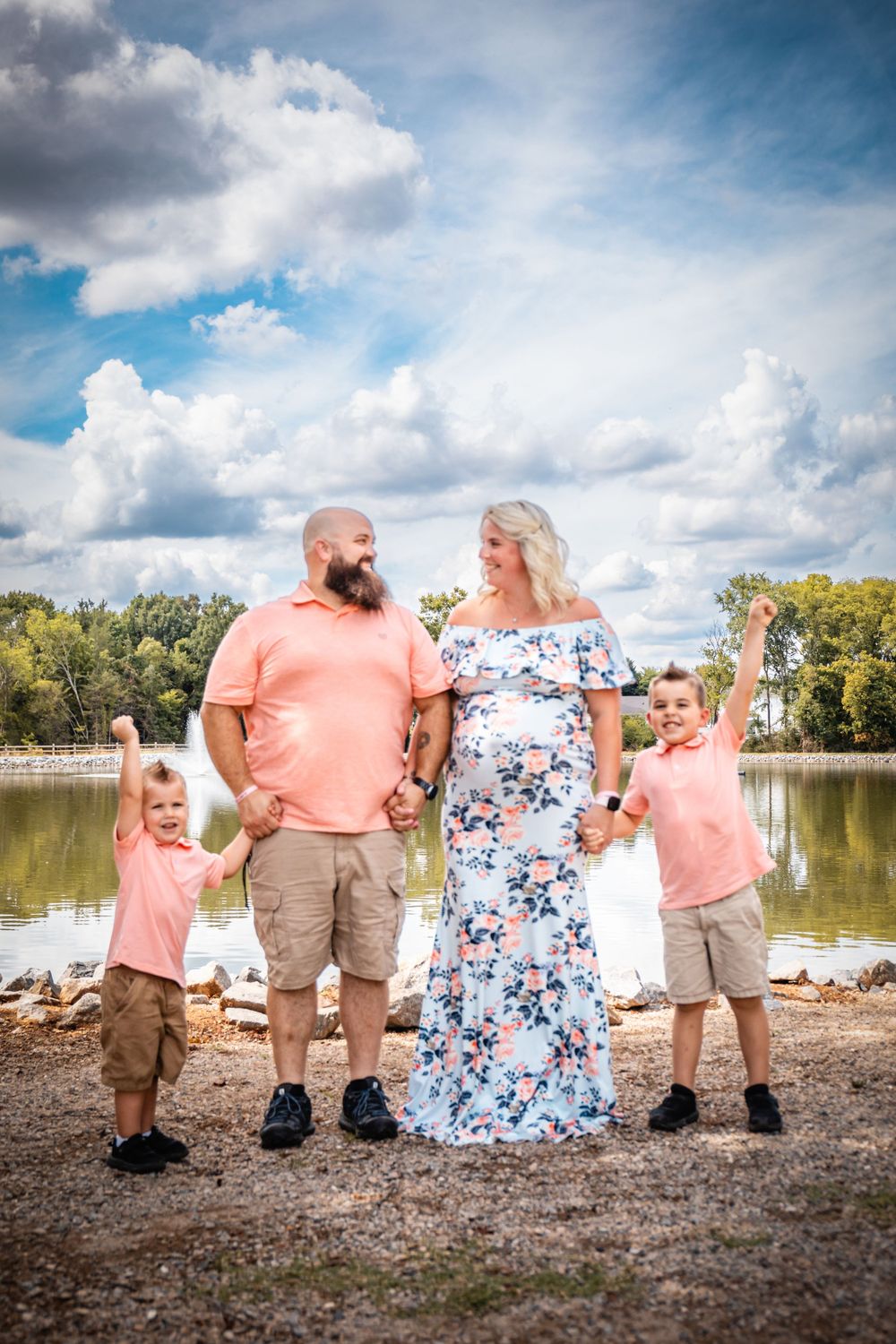 A family photo session by a lake with coordinated coral and floral outfits.