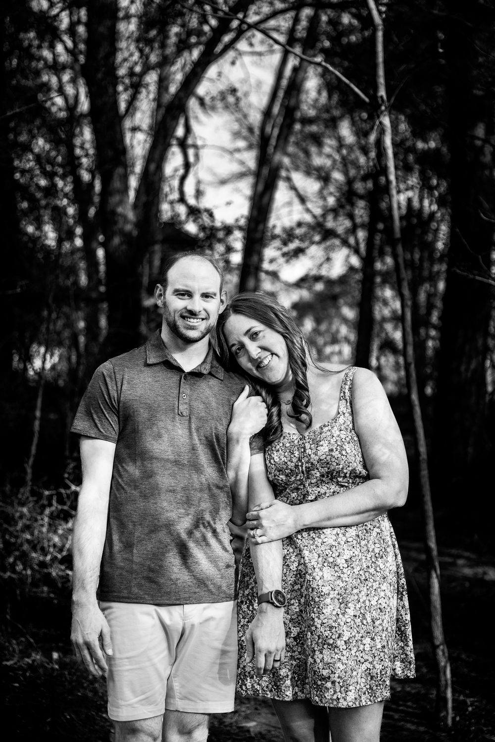 Happy couple posing together in a black and white portrait surrounded by trees in a forest.