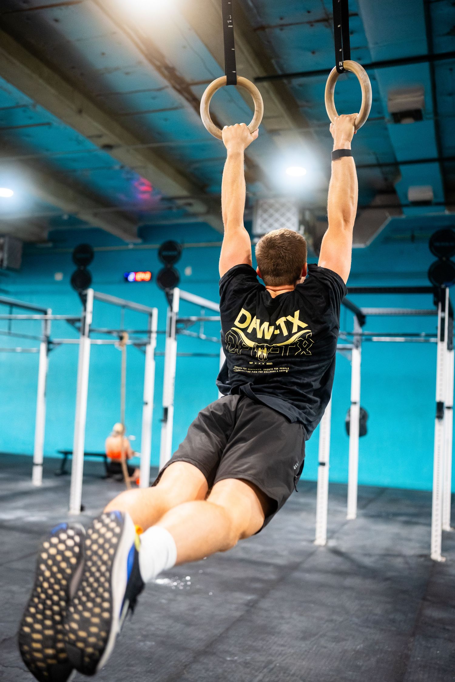 Athlete performs gymnastic ring exercises in CrossFit gym with blue lighting.