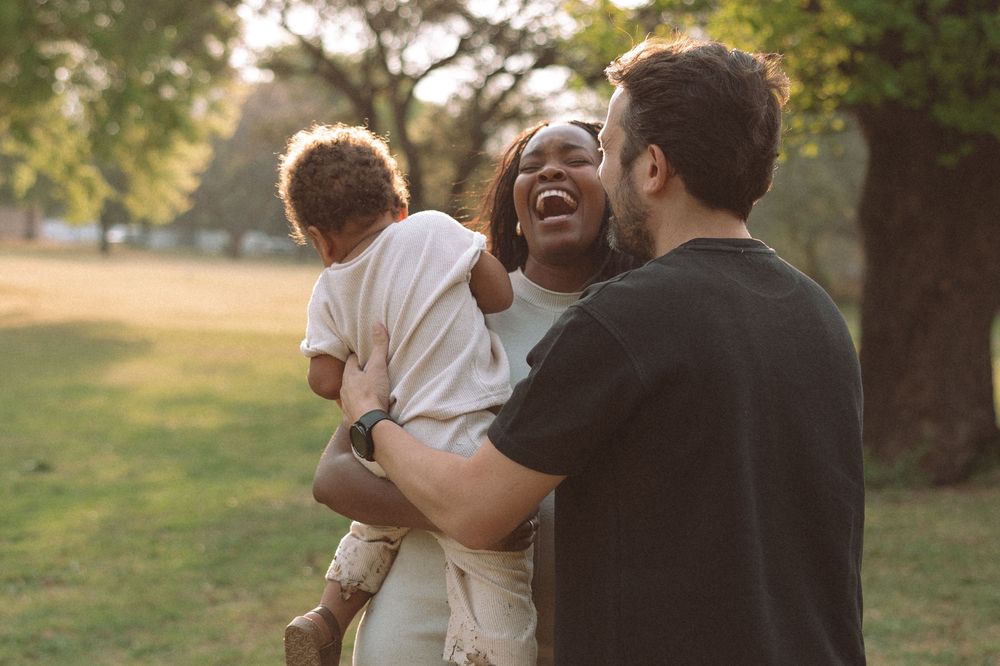 A couple embraces and laughs together in a sunlit outdoor setting during a romantic photoshoot.