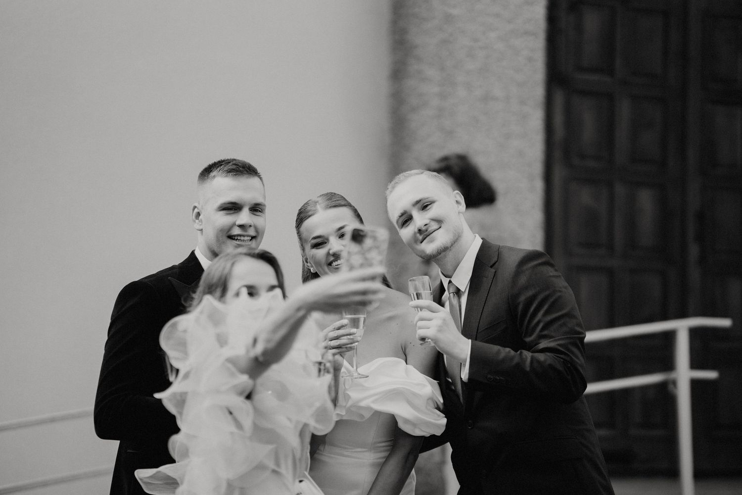 Wedding party sharing celebratory drinks and laughter in black and white.