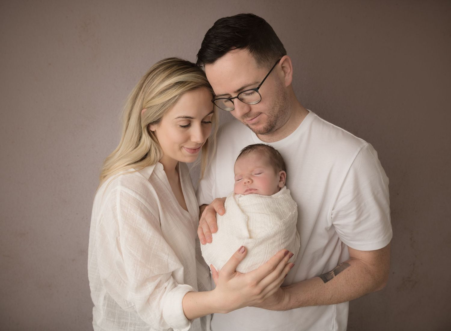 A series of seven intimate family portraits showing tender moments between parents and their newborn baby in soft lighting.