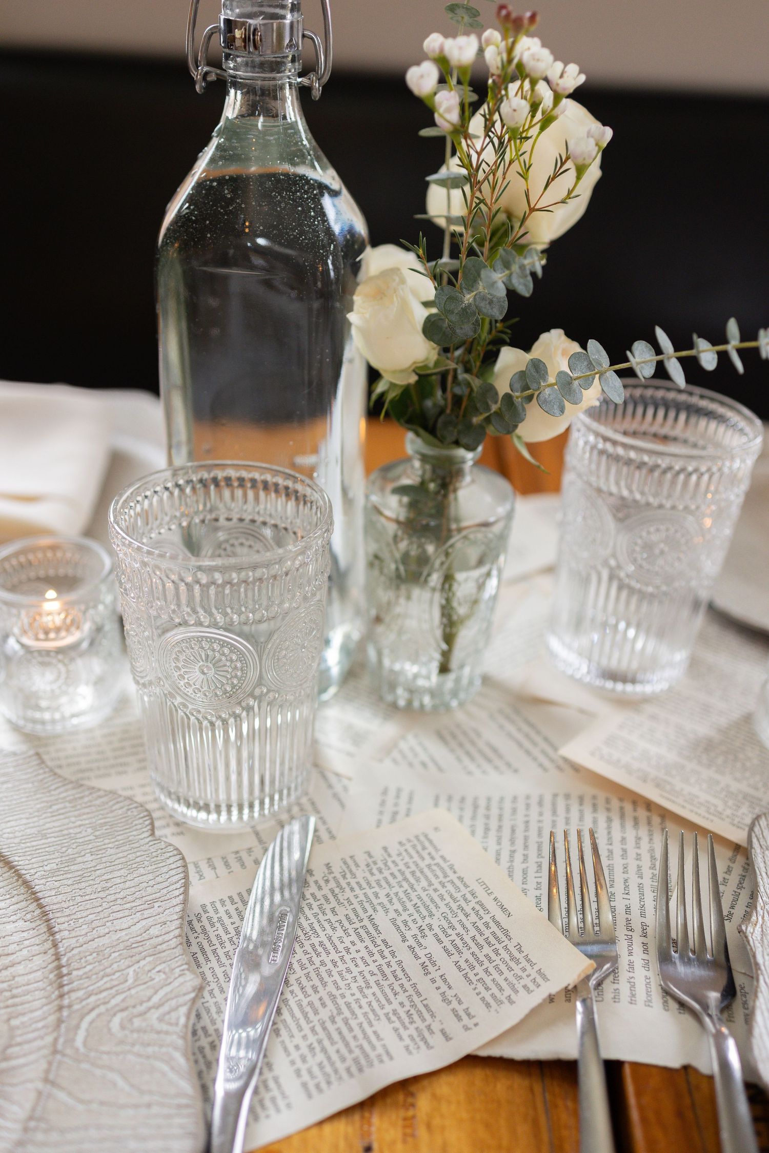 Vintage-inspired place settings with cut glass goblets and white roses on book page tablecloths.