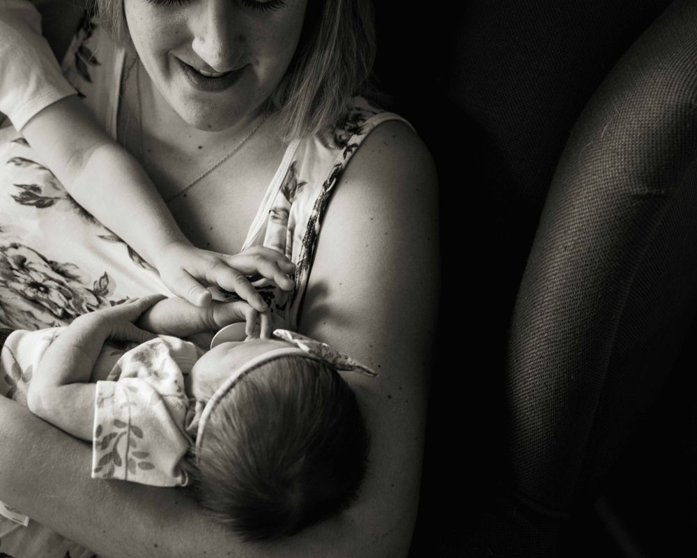Intimate black and white image of mother nursing newborn in soft natural light.