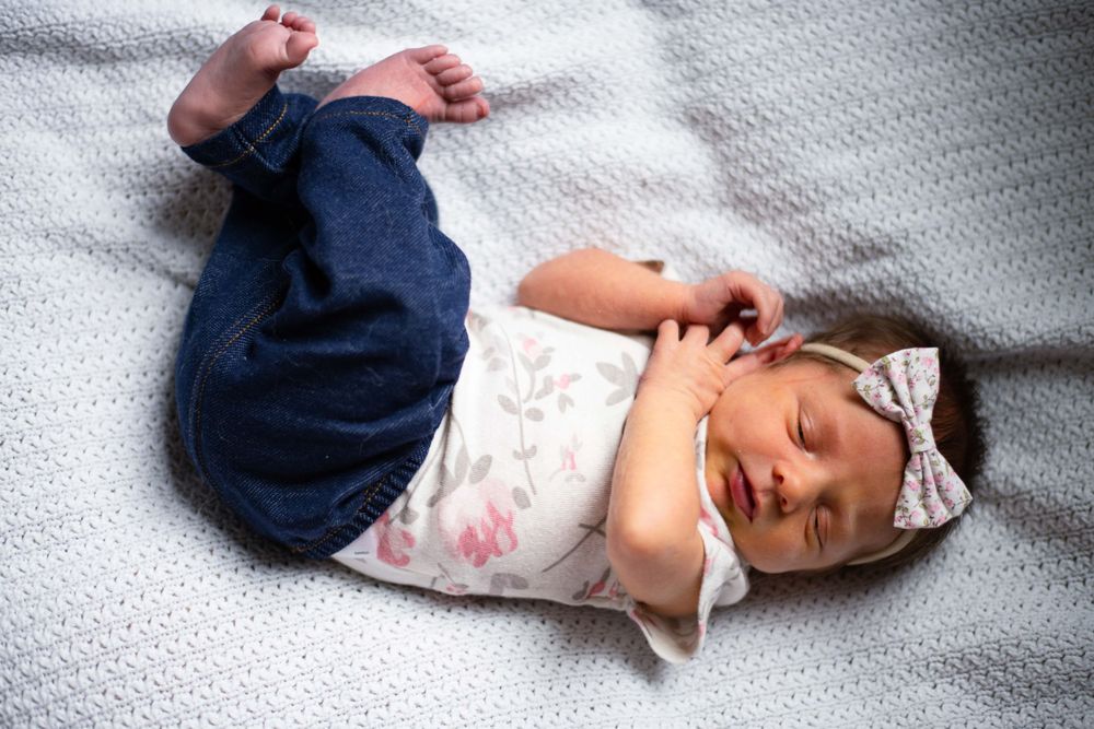 Happy baby in floral top and navy bottoms laying on grey blanket.