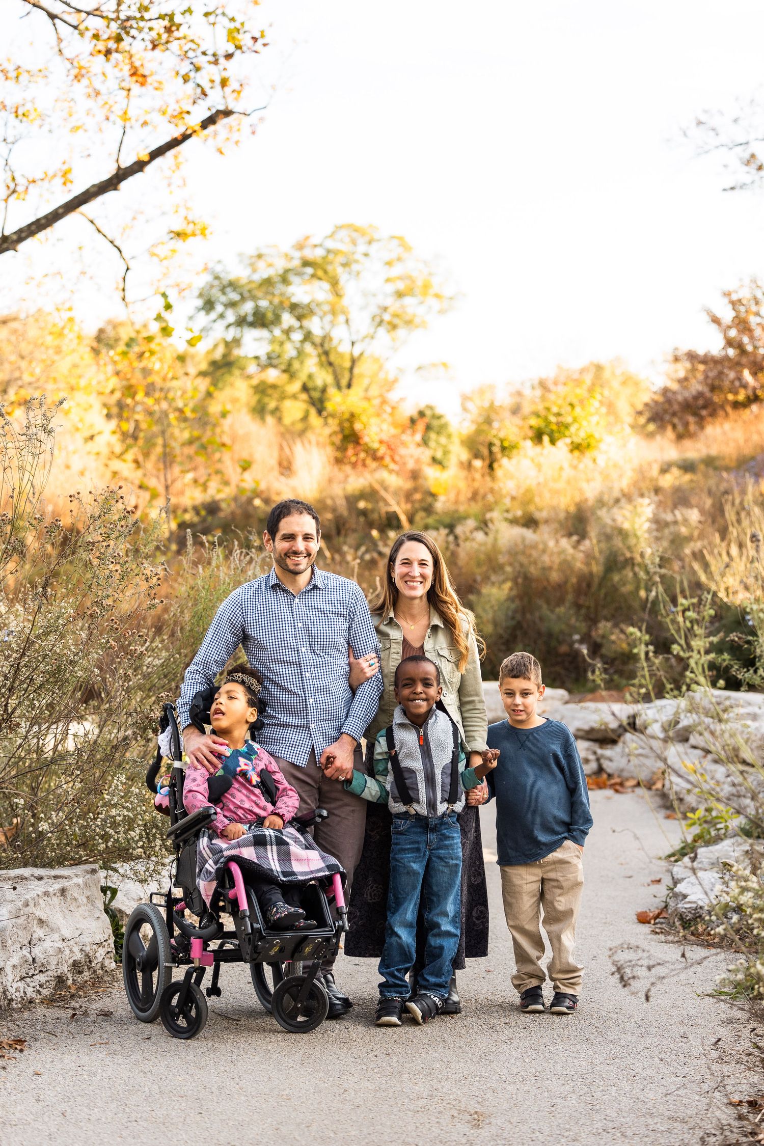 Family portrait on a natural path with wheelchairs and autumn scenery in the background.