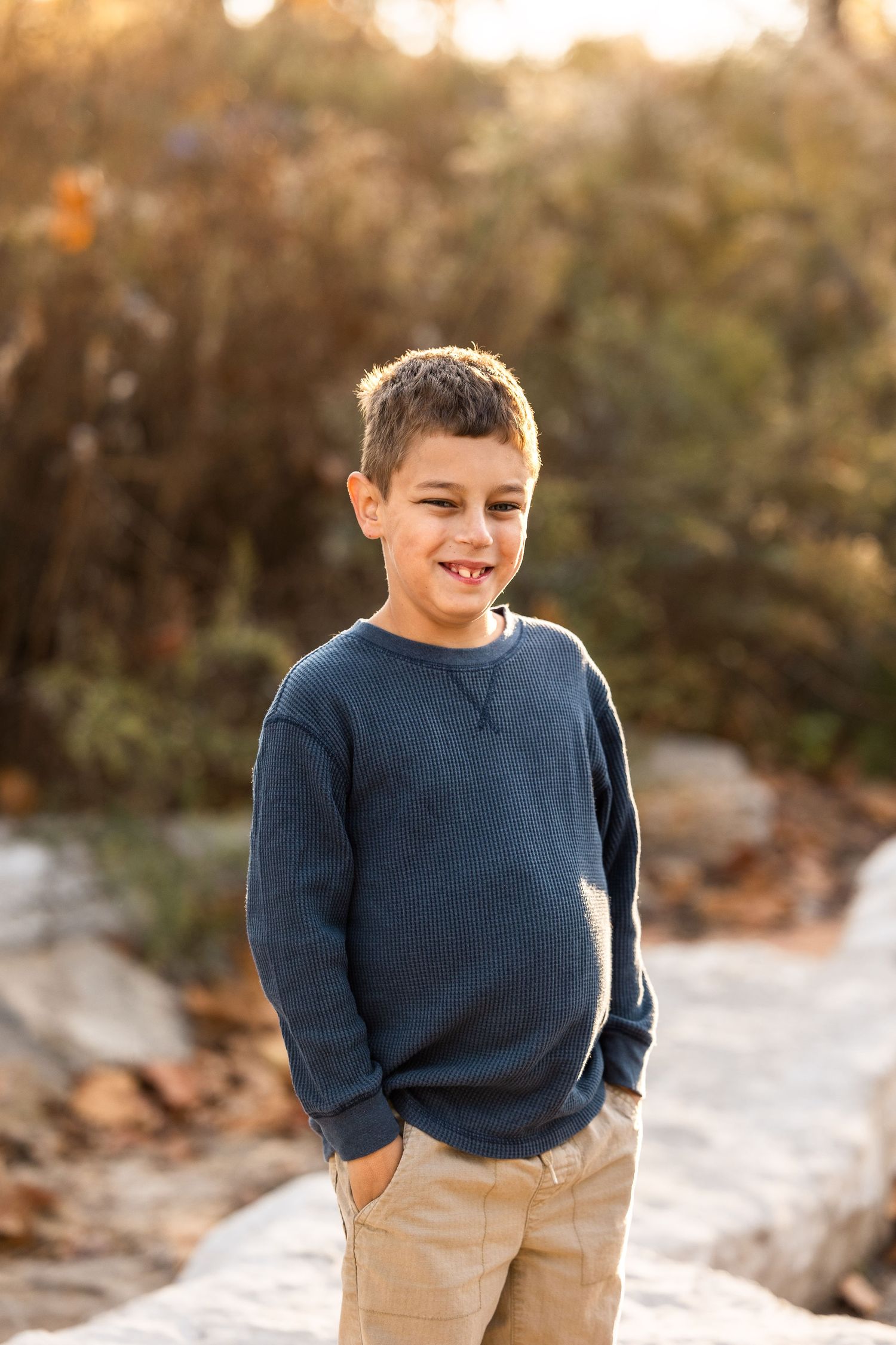 Child in blue sweater laughing and playing outdoors during golden hour photoshoot.