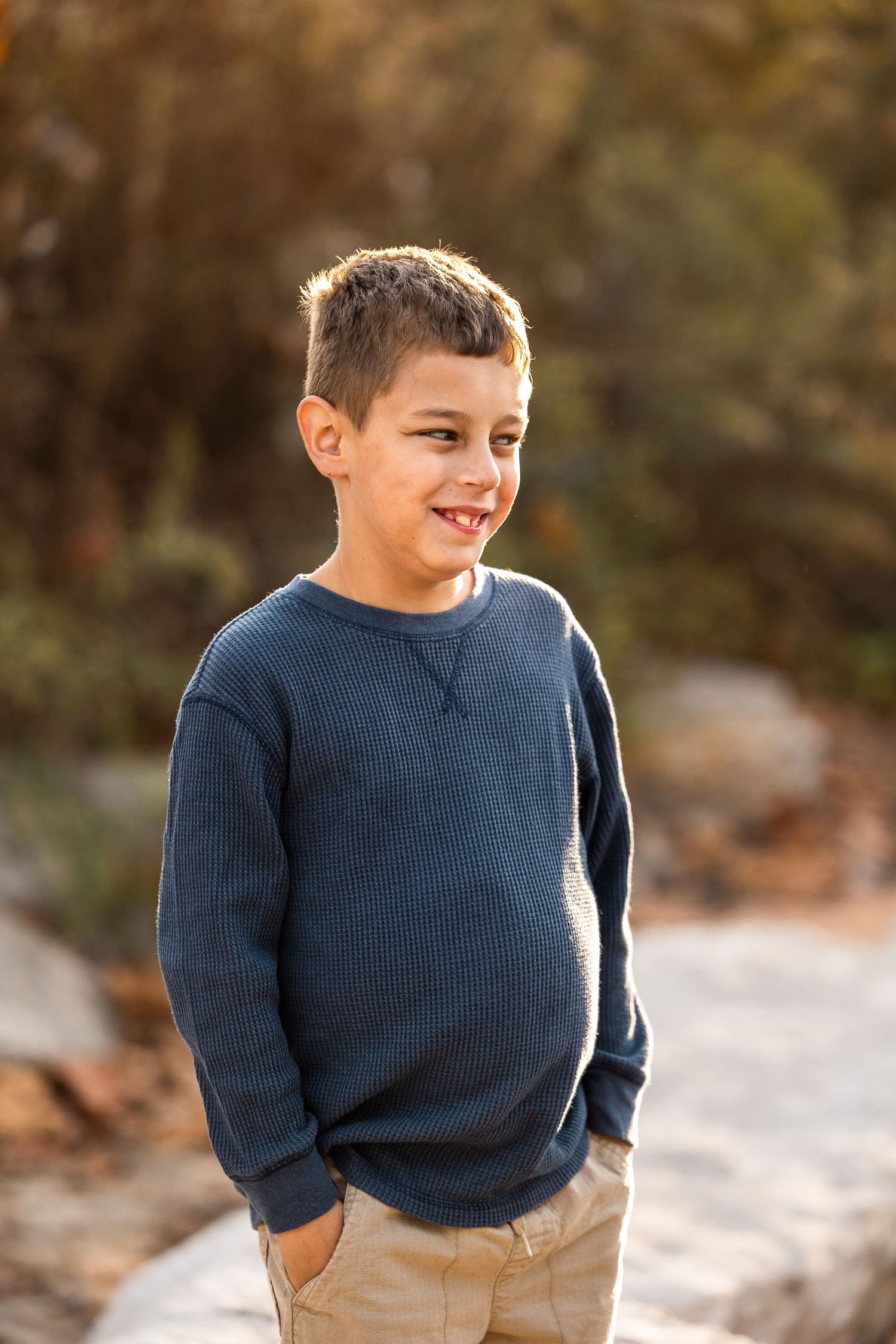 Young child in navy sweater and khaki pants standing outdoors during golden hour.