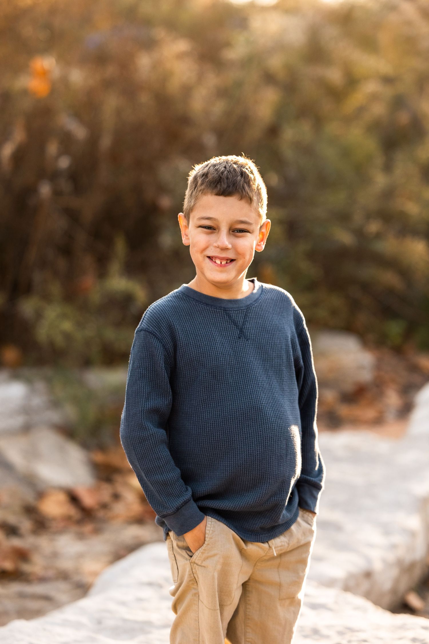 Child in navy sweater and khaki pants smiling and playing outdoors during golden hour.