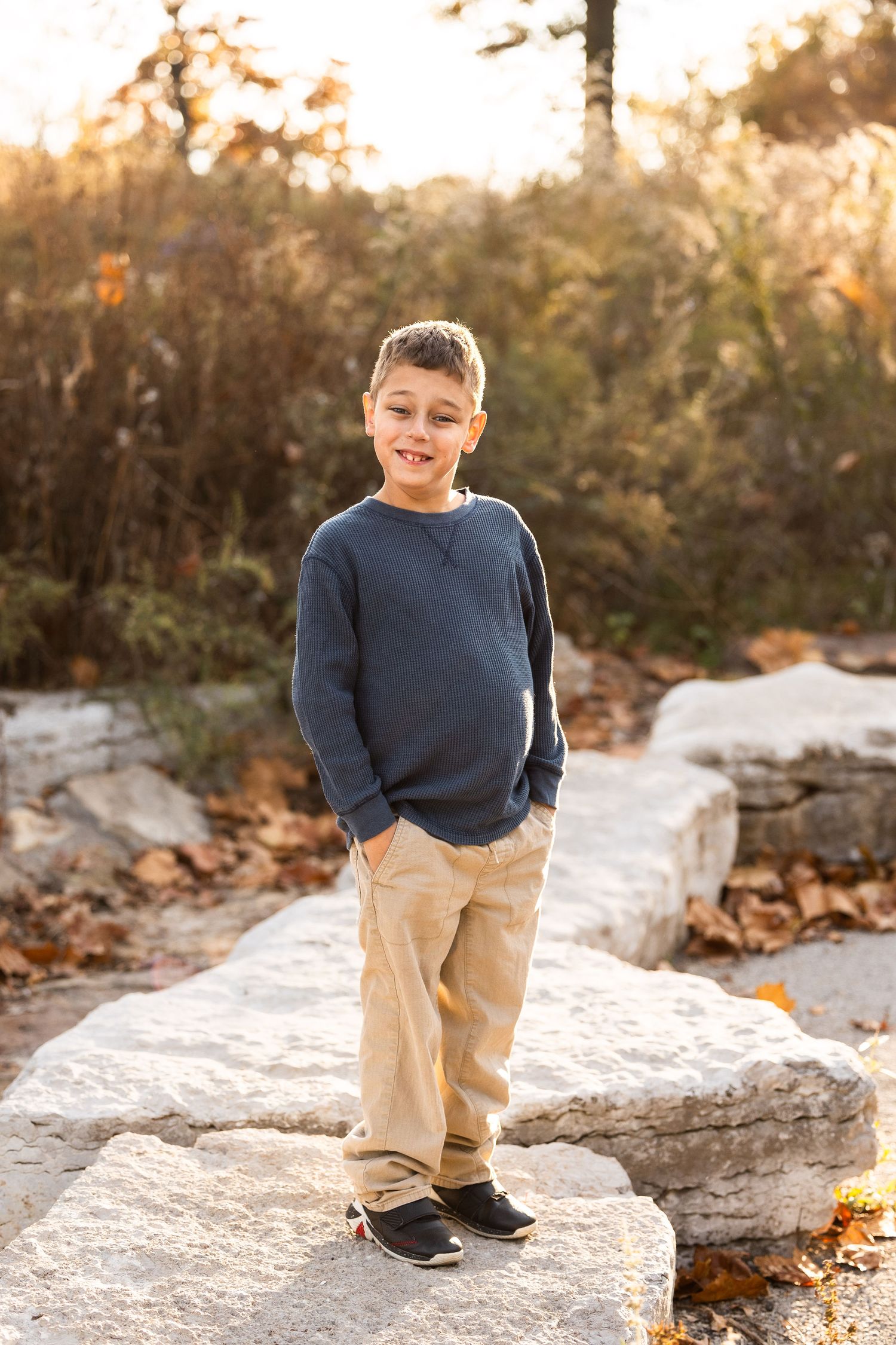 Child in blue sweater standing on rocky terrain at sunset.