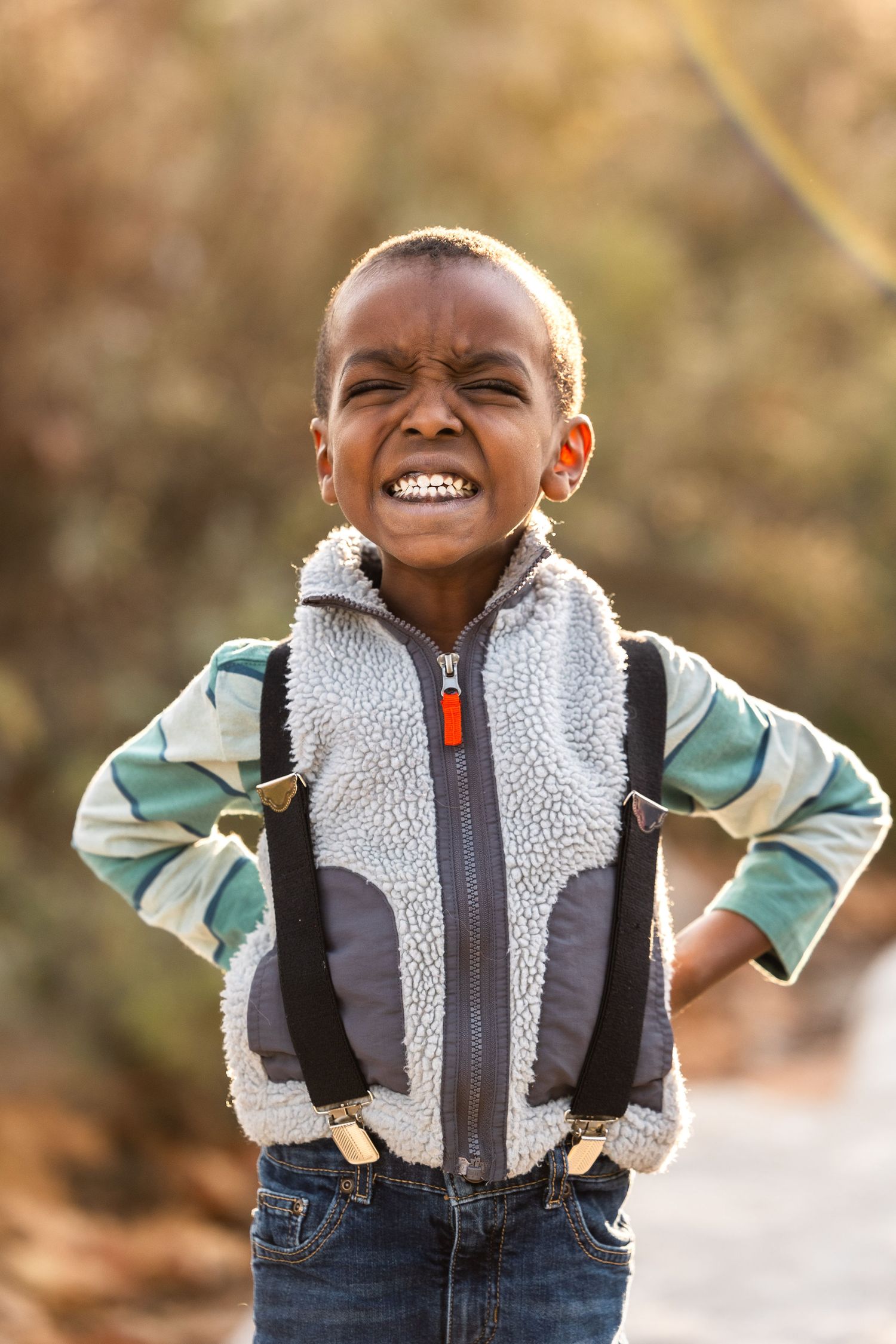 Child wearing a sherpa vest and green shirt smiling joyfully outdoors.