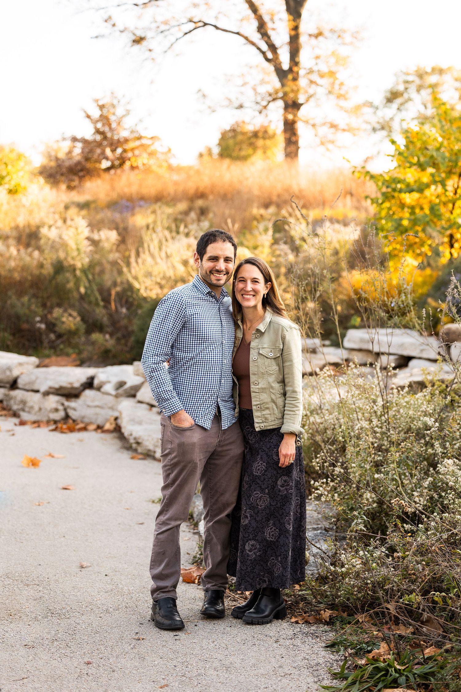 Couple posing together on nature trail during golden hour with fall foliage in background.