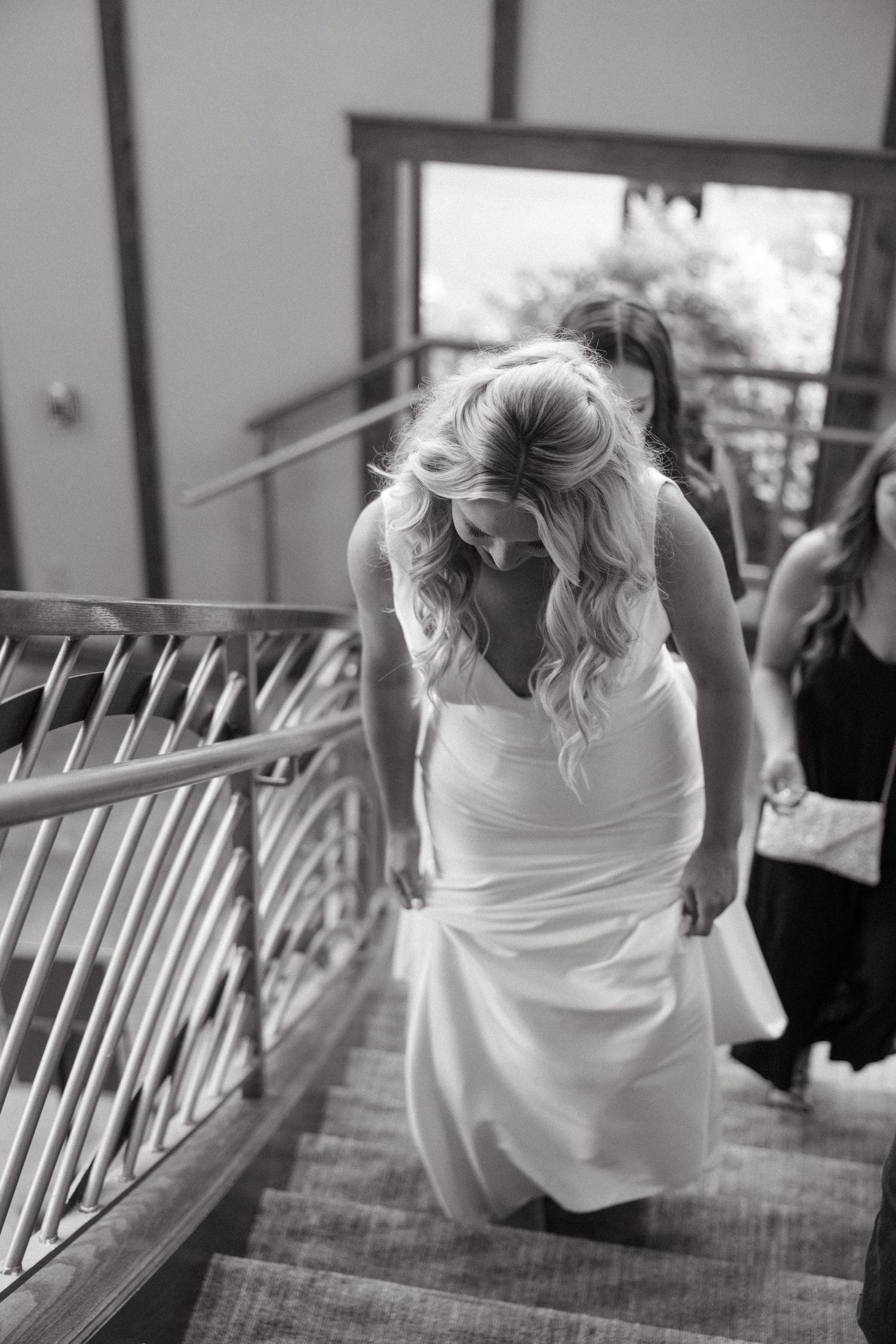 Black and white photo of bride descending staircase in fitted white wedding gown.