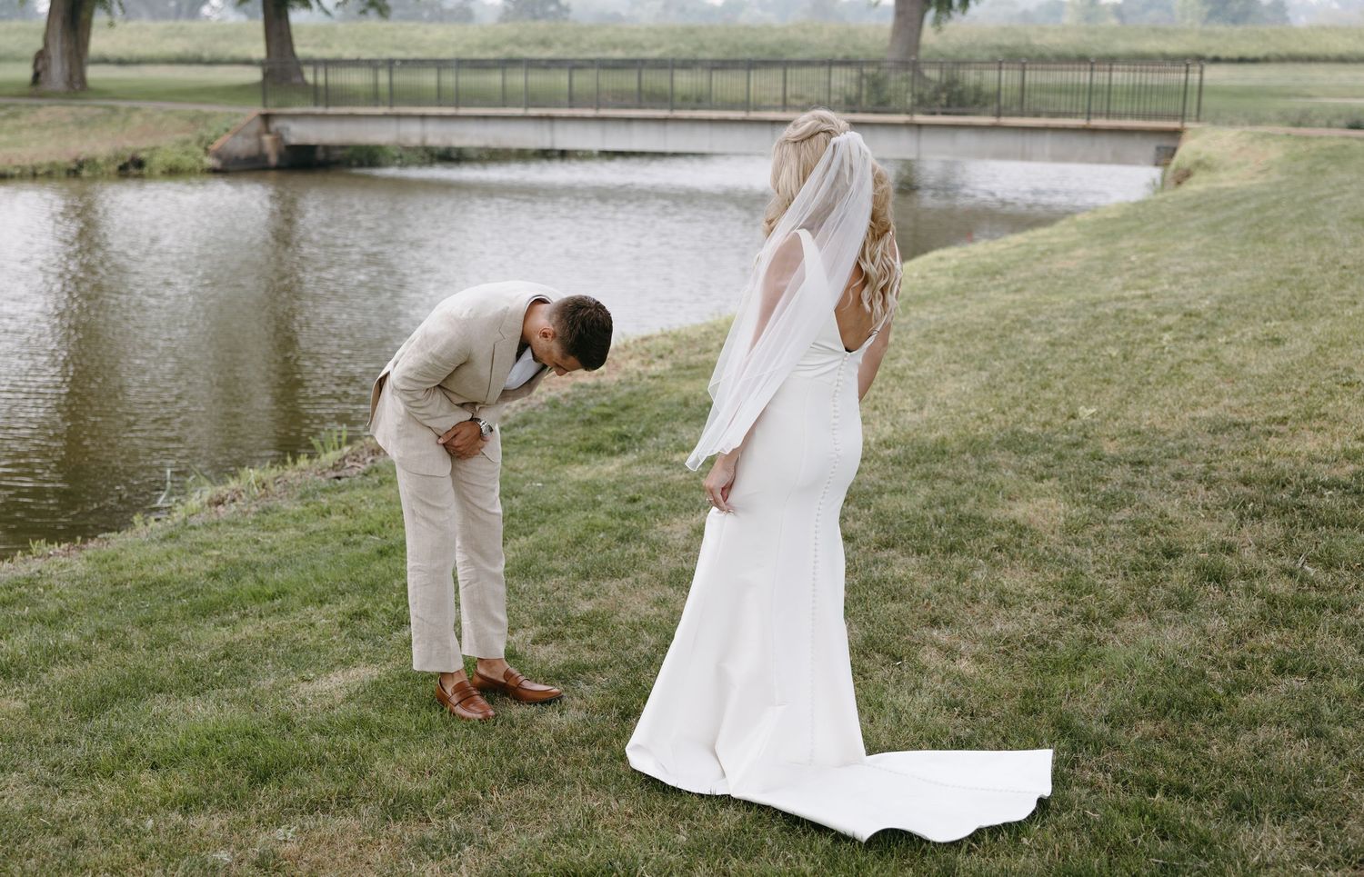 Candid first look moment between bride and groom by pond with walking bridge.
