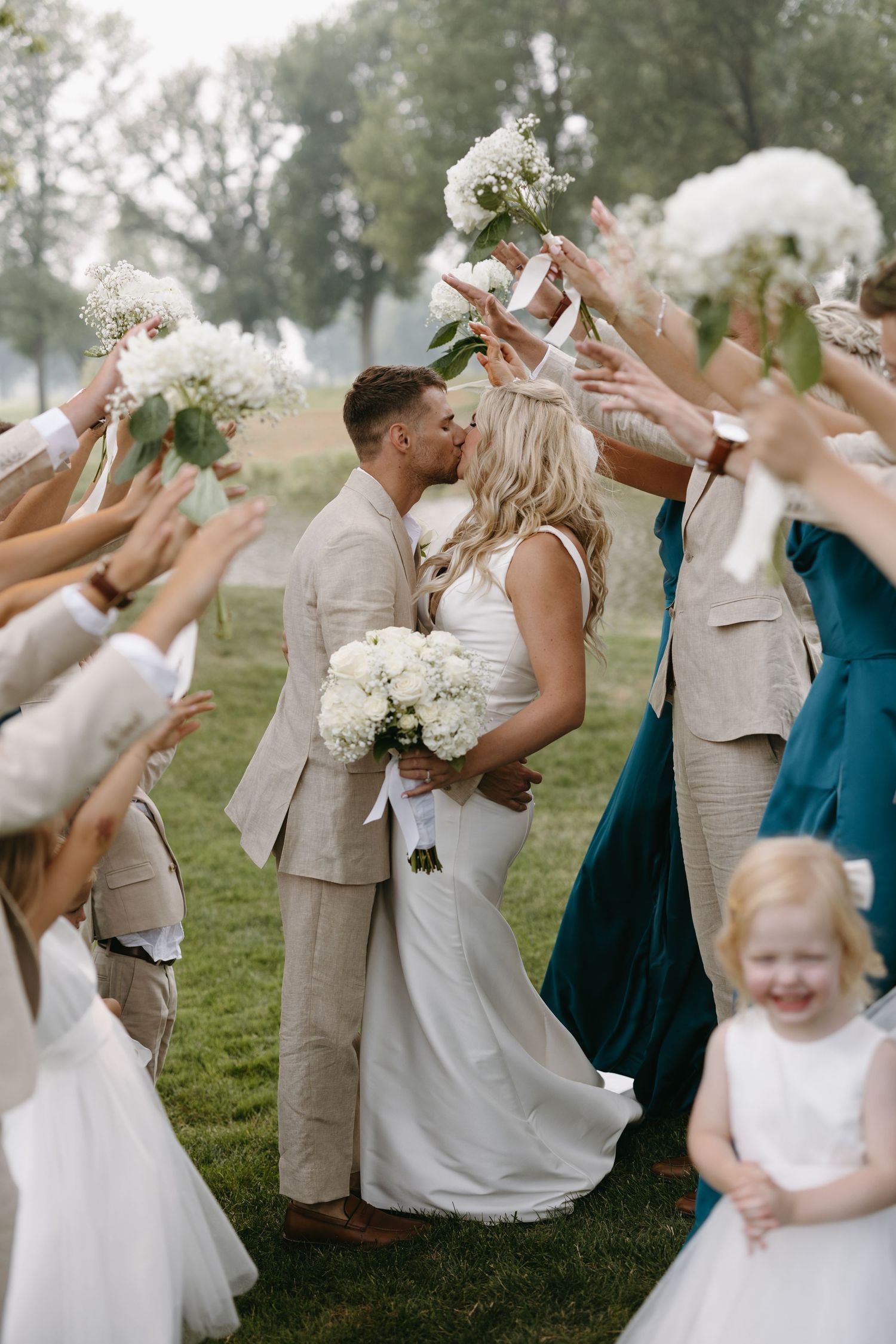 Wedding couple shares kiss during flower petal toss celebration on golf course.