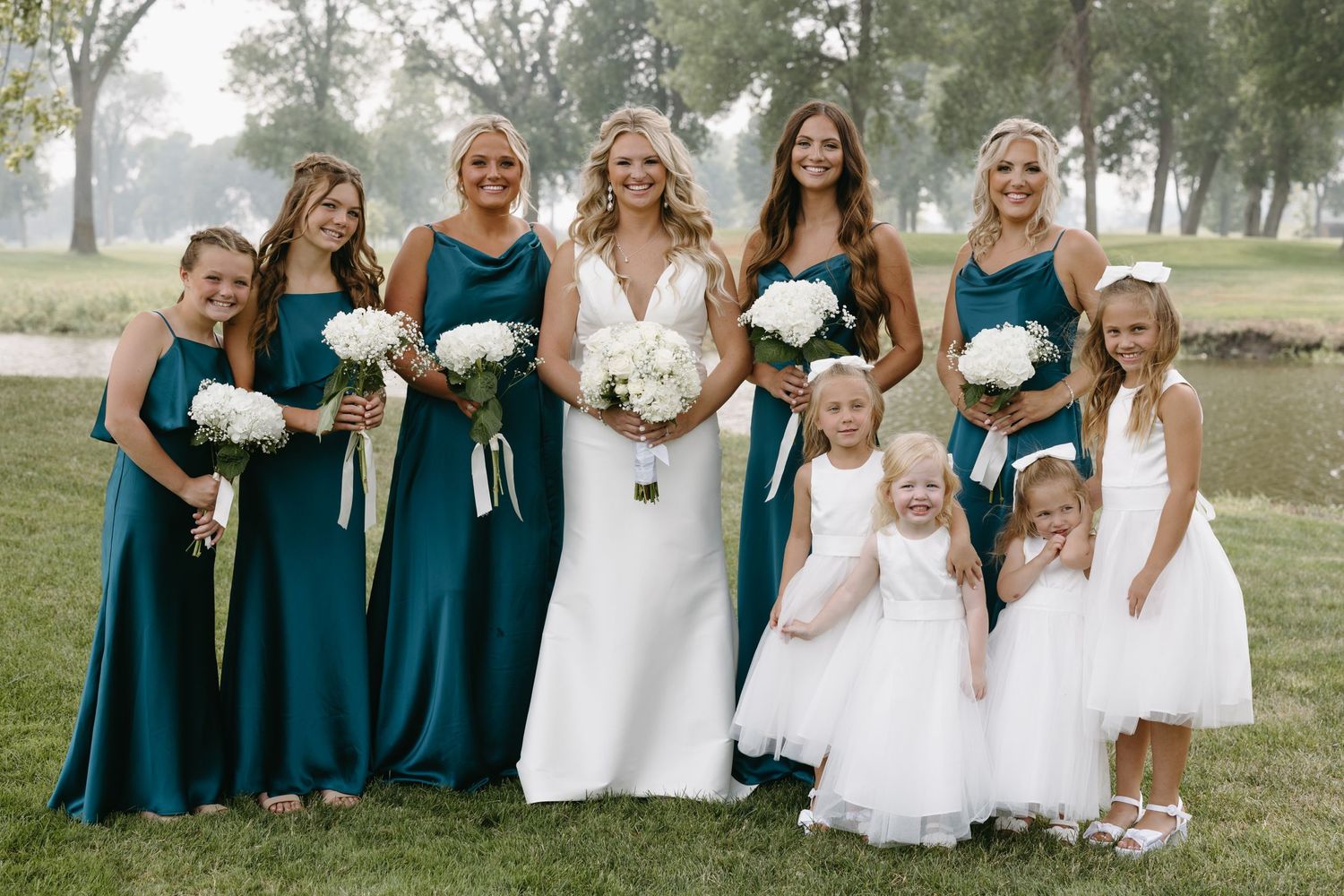 Wedding party group photo with bridesmaids in teal dresses and flower girls in white.