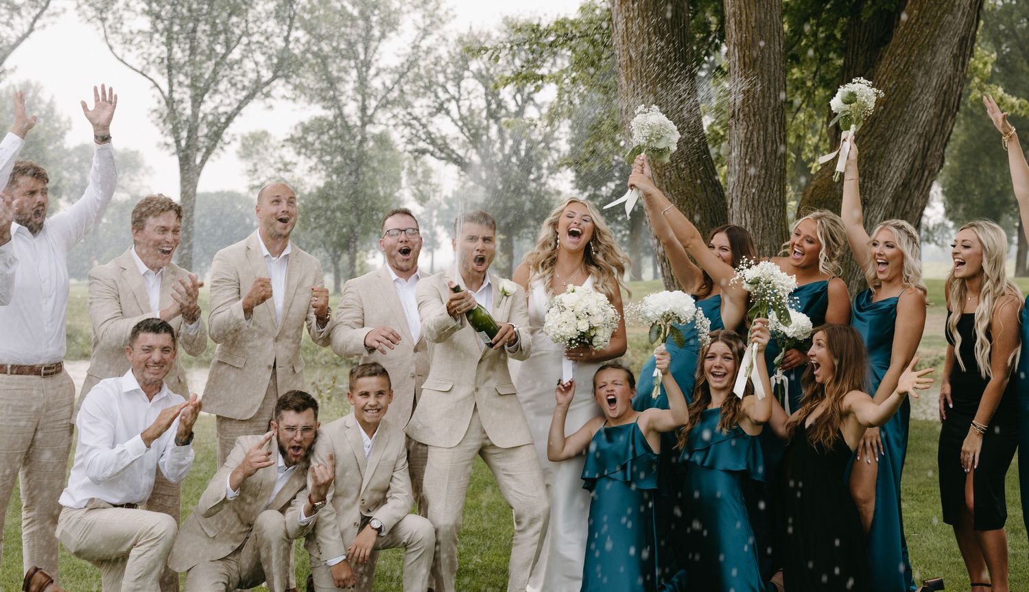 Wedding party throws confetti during celebratory group photo on golf course.