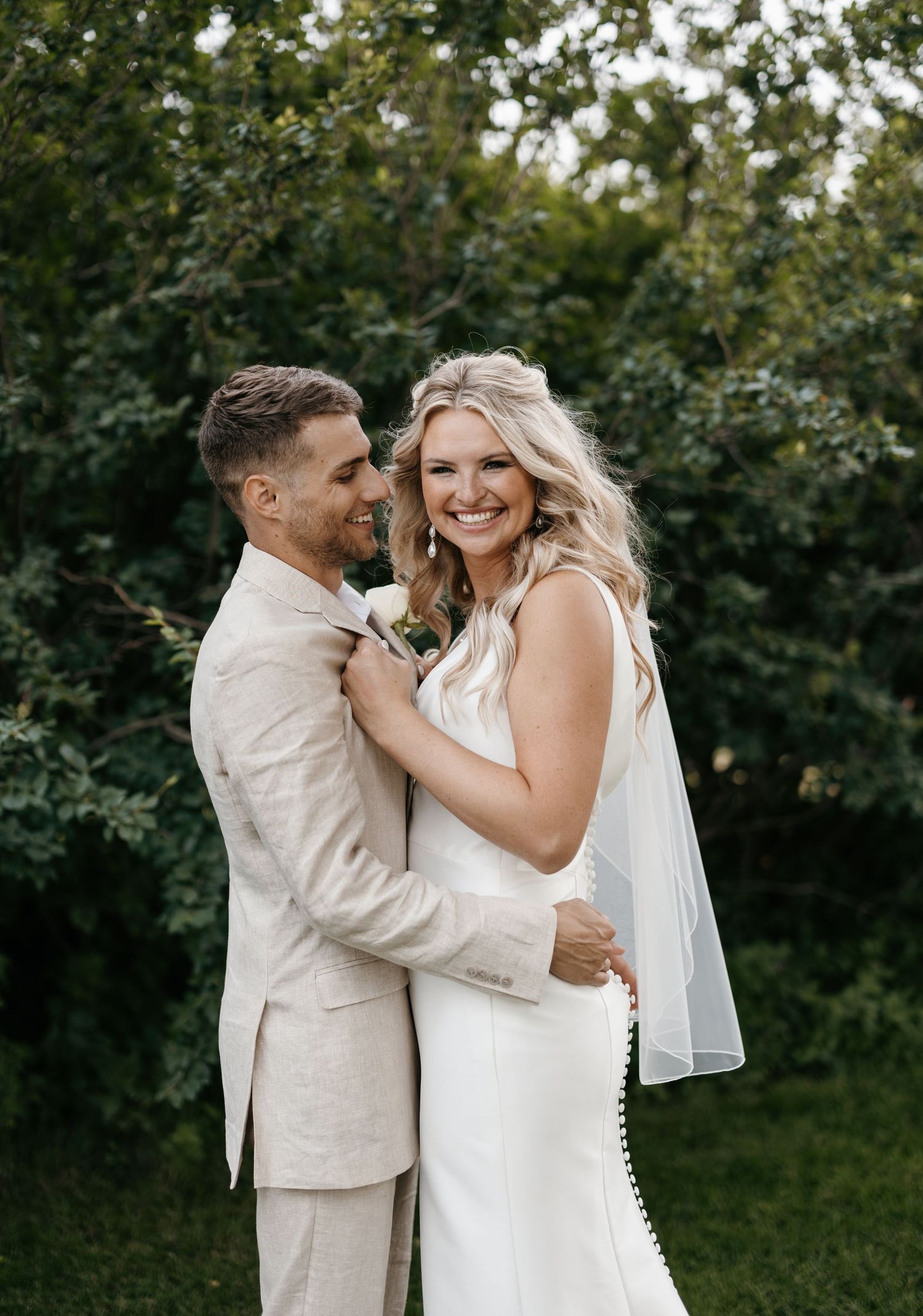 Romantic outdoor wedding portrait of couple in beige suit and white dress.