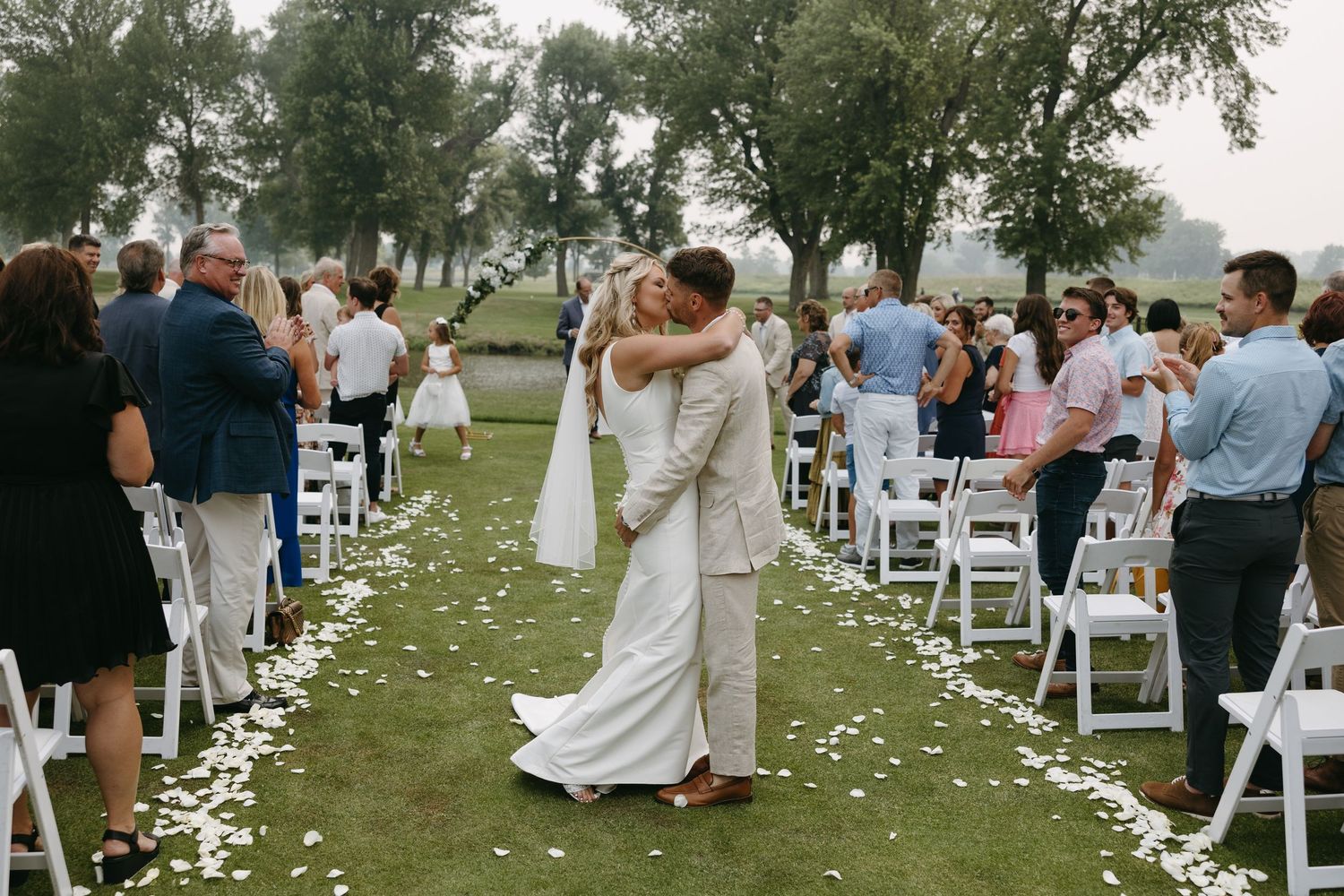 A wedding celebration with guests watching a newlywed couple's first dance along a petal-strewn aisle.
