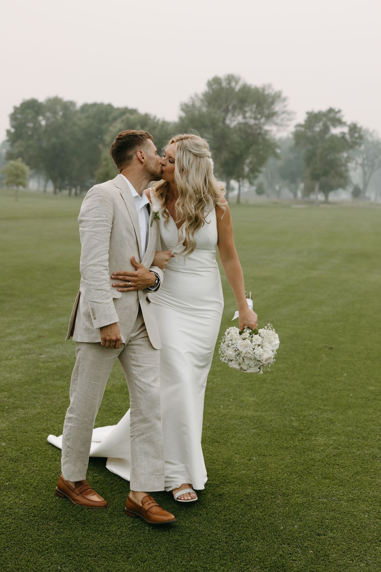 A tender moment between newlyweds in light-colored attire on a misty golf course.