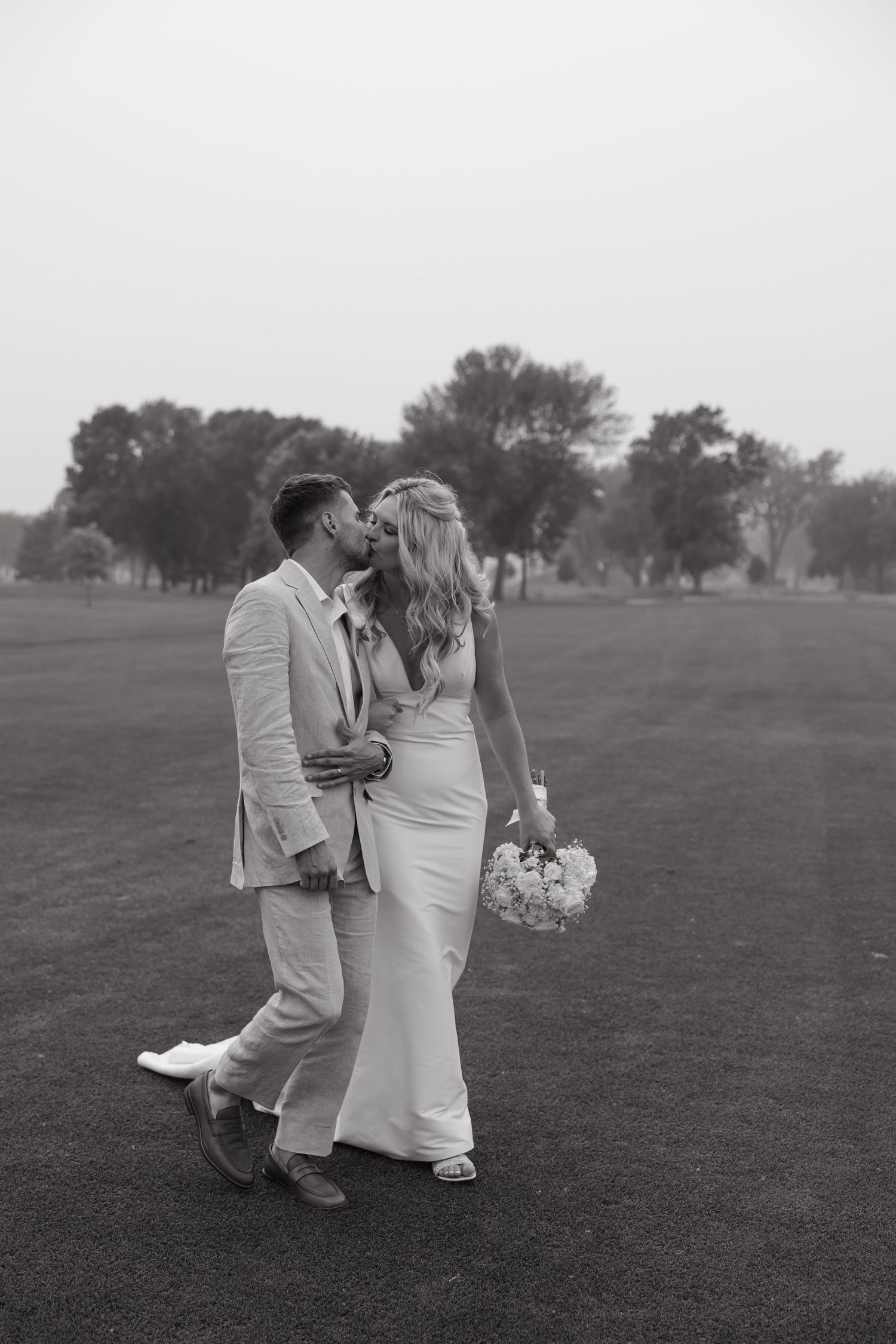 A romantic black and white portrait of newlyweds embracing on a golf course.