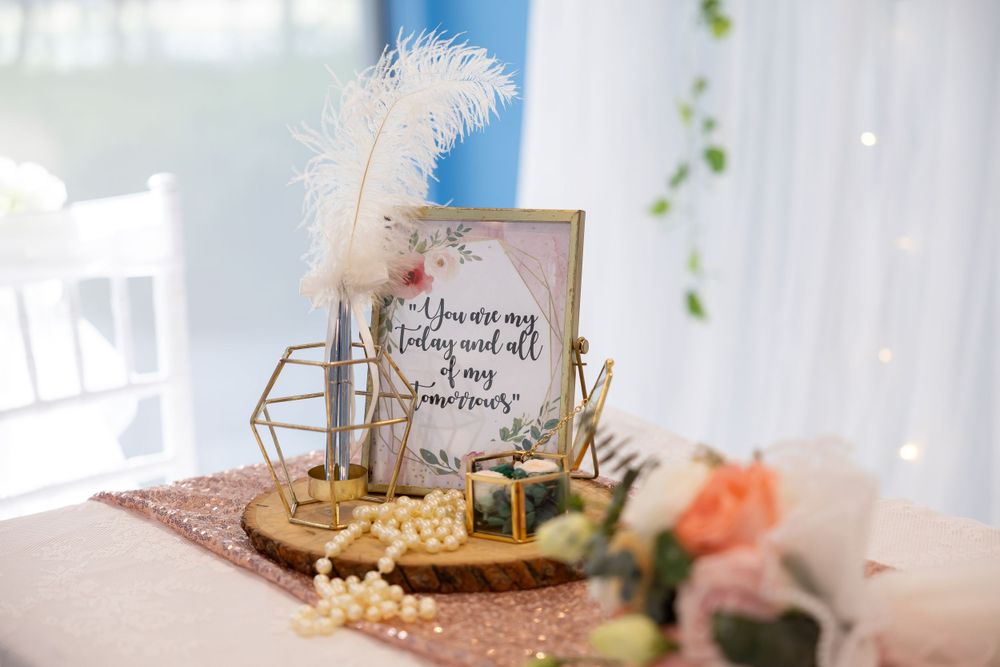 Vintage wedding decor with feathers, pearls and framed quote on rose gold tablecloth.