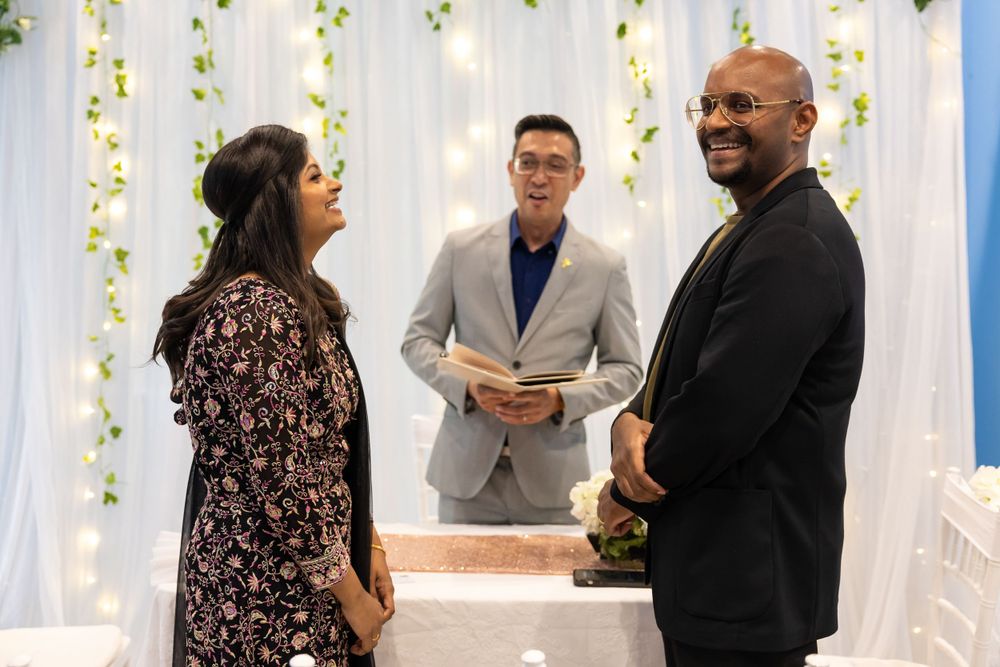 Wedding ceremony in progress with white floral backdrop and guests seated.