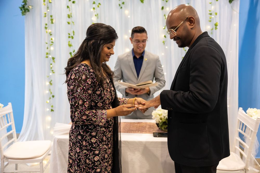 Wedding ceremony ring exchange moment with officiant and floral backdrop.