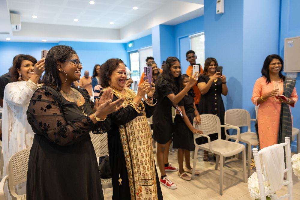 A group celebrates joyfully in a room with bright blue walls and white chairs during a special occasion.
