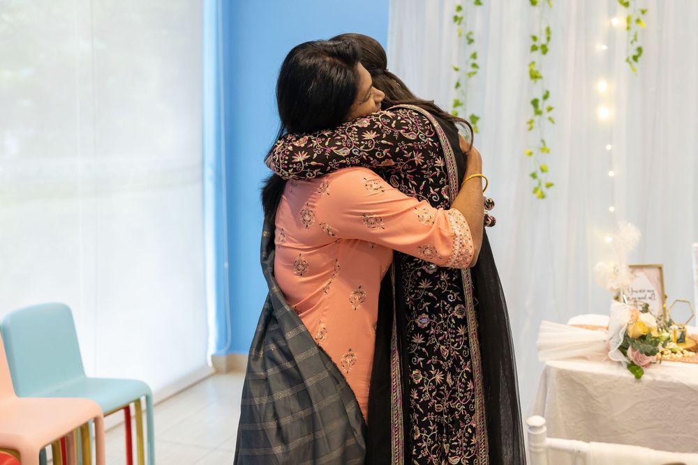 Two people share a warm embrace at an event decorated with floral accents and string lights.