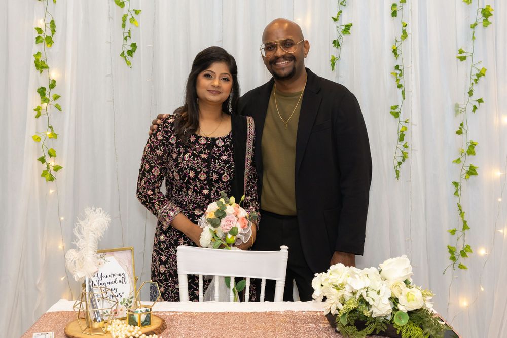 A couple poses together at a decorated event setting with white flowers and string lights.