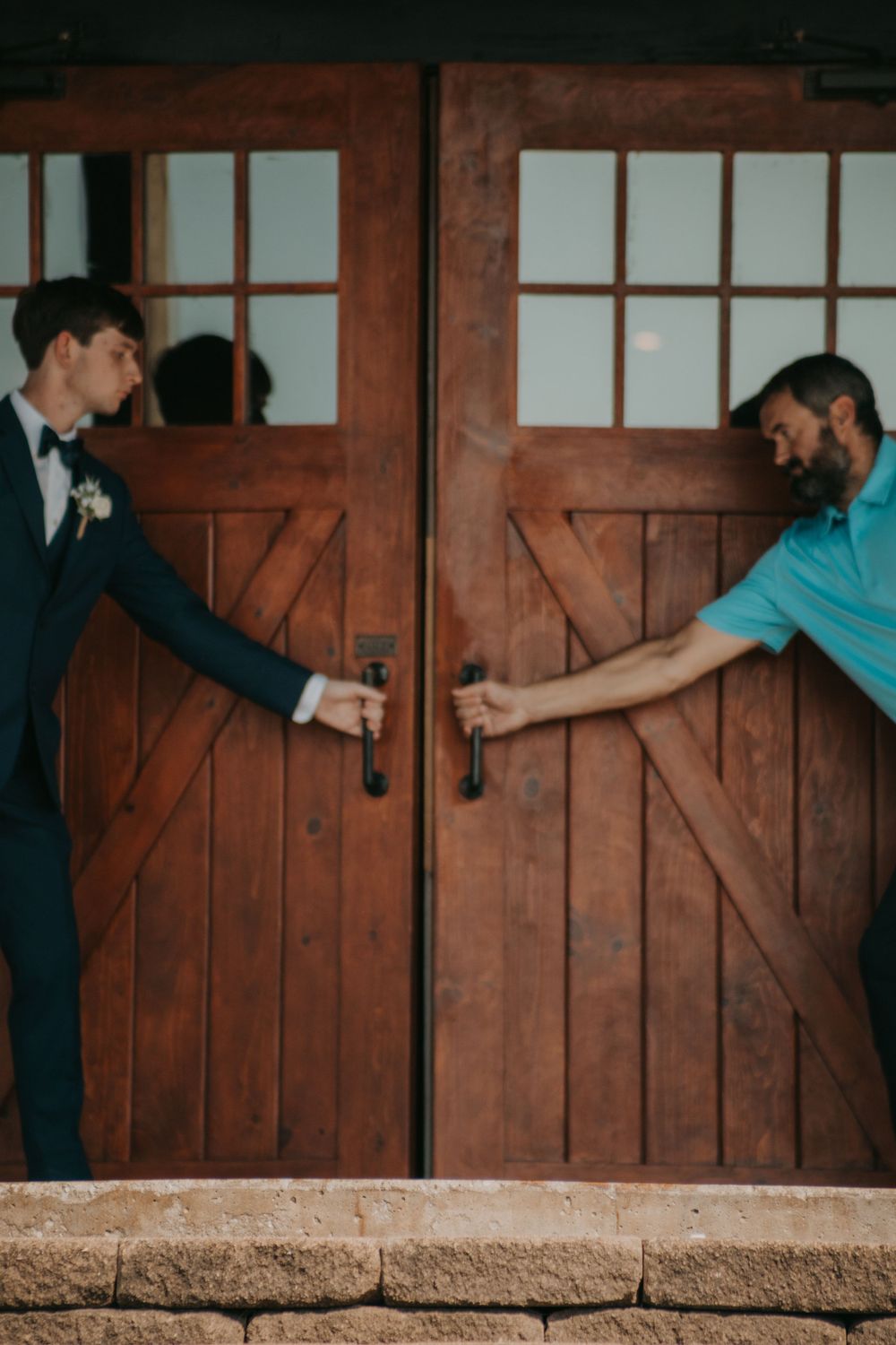 Two people playfully reach for door handles on rustic wooden barn doors.
