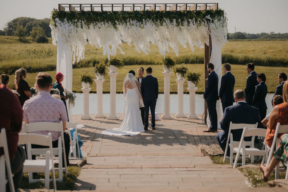 A wedding ceremony takes place under a white pergola decorated with flowing fabric and florals.