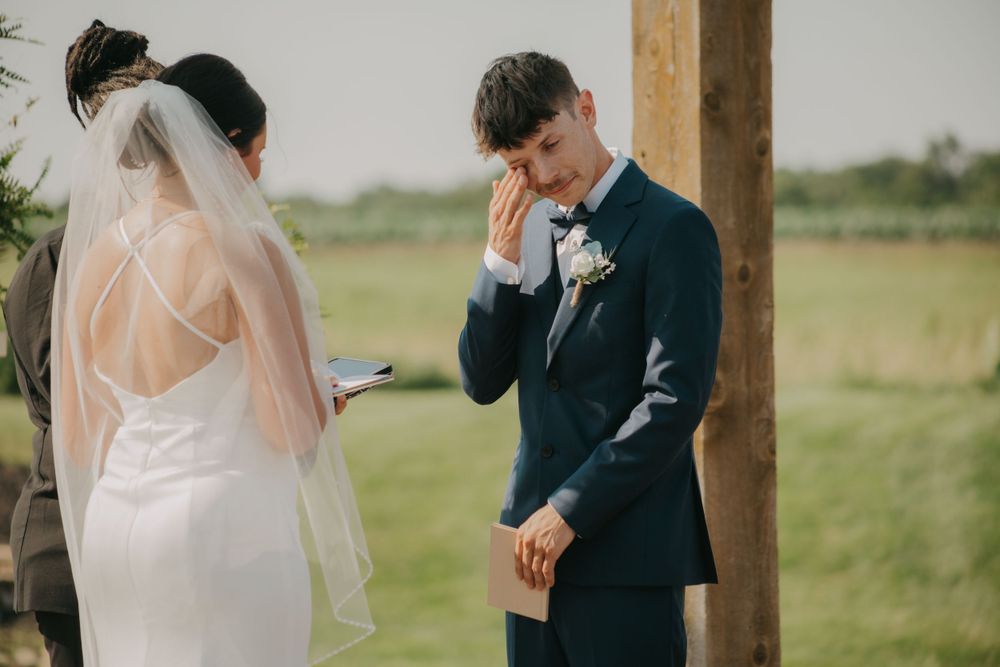 An emotional moment during wedding vows as a couple stands under a wooden pergola.