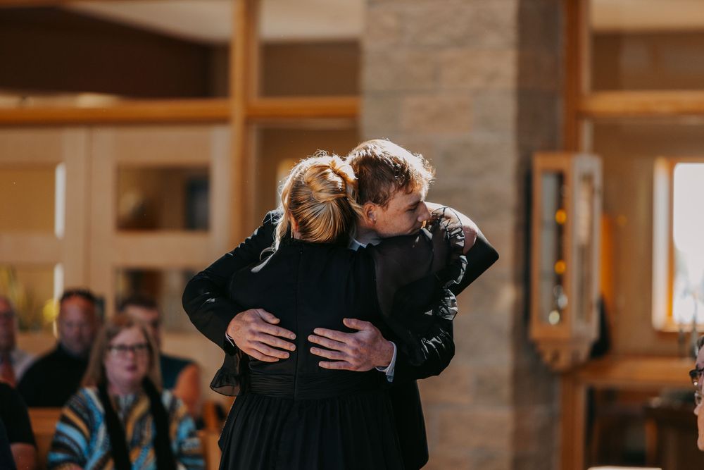 Two people share a tender embrace while dancing together in an indoor venue with stone pillars and warm lighting.