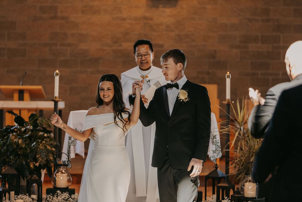 Wedding party dances and celebrates during reception in rustic brick-walled venue with warm lighting.