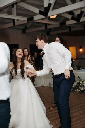 A couple shares a joyful dance together on a wooden floor at their wedding reception.