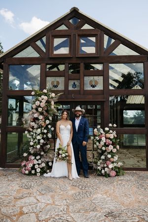 Wedding couple poses at rustic barn venue with wooden beams and floral arch decorations in pink and white.