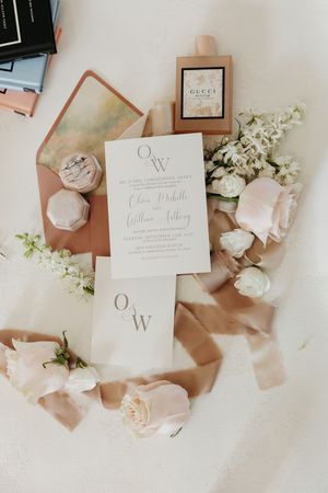 Elegant wedding invitation suite with white cards, blush pink roses, and silk ribbons arranged on a neutral surface.