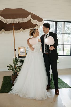 Wedding couple posing under a vintage brown umbrella in a bright indoor setting with greenery.