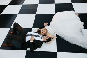 Artistic overhead view of couple on black and white checkered floor with flowing white dress.