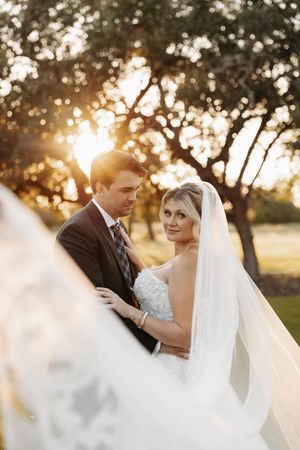 Romantic wedding couple embraces during golden hour sunset with trees silhouetted in background.