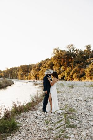 A romantic sunset photoshoot along a rocky riverbank with autumn trees glowing in golden light.