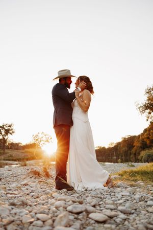 Dreamy wedding photos on a rocky shore with dramatic sunset backlighting and natural scenery.