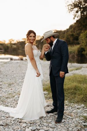 Newlywed couple poses along rocky riverbank at sunset in romantic wedding photos.
