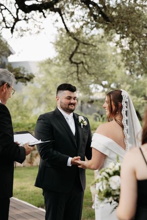 A couple exchanges vows during an outdoor wedding ceremony under oak trees on a beautiful spring day.