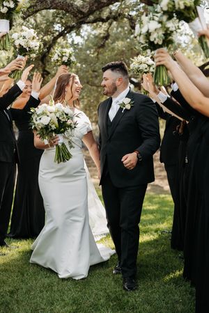 Wedding party in black and white attire celebrates joyfully on a grassy lawn during an outdoor celebration.