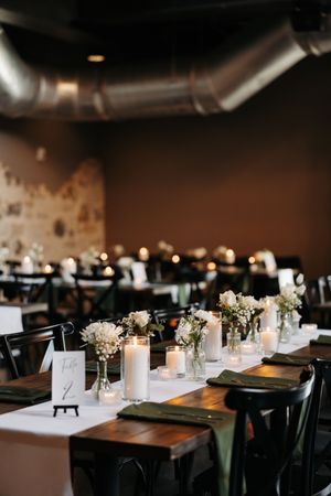 Elegant restaurant table settings with wooden tables, black chairs, and delicate white floral centerpieces with glowing candles.