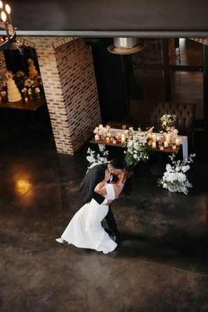 Romantic wedding couple shares an intimate dance dip on a dark floor against exposed brick walls lit by candlelight.