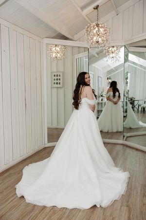 A bride in a flowing white ballgown twirls gracefully in an elegant white room with crystal chandeliers and hardwood floors.